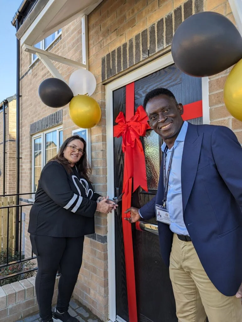 A new housing development opened a couple that have the keys celebrating with a red ribbon on the door and balloons